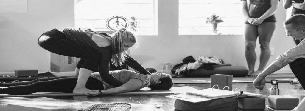 a yoga teacher adjusts a student in a yoga class